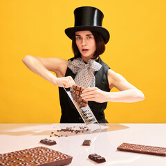 Artistic, beautiful woman in cylinder hat grating chocolate on grater against yellow background....