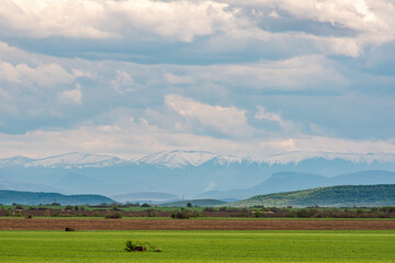 Obraz na płótnie Canvas Arable fields in the spring in the Danubian plain in the background is the Central Balkan, the highest part of the Balkan Mountain (Stara Planina) with peaks covered with snow, Bulgaria, Europe.