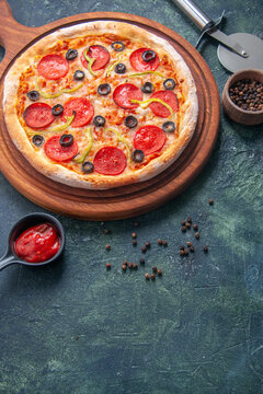 Delicious pizza on wooden cutting board and pepper ketchup on isolated dark background in vertical view