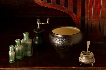 Kitchen interior: glass bottles, a cauldron for the oven, a metal sugar bowl on a wooden sideboard.