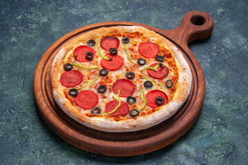 Delicious pizza on wooden cutting board on dark blue background with free space in close up shot
