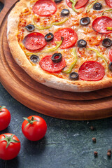 Homemade pizza on wooden cutting board and tomatoes on isolated dark background