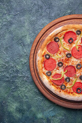 Tasty pizza on wooden cutting board on the left side on isolated dark background with free space