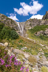 Majestic beautiful bright summer view of the mountain peaks and the Shdugra waterfall, Mazeri in the mountains of Upper Svaneti, Georgia. Conceptual background of the beauty of nature. Verttical photo