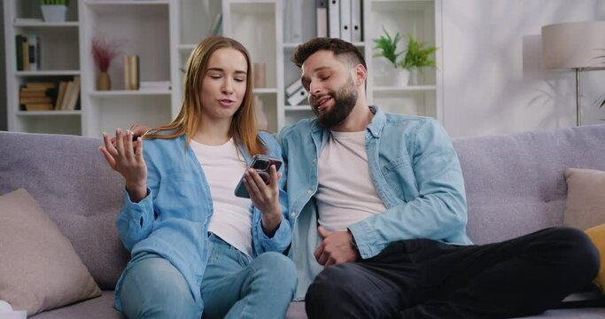 Young couple woman and man smiling looking at smart phone. Boy and gir shopping on internet, watching funny videos, use social media, streaming service.