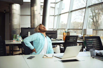 Male in hat massages his lower back at work