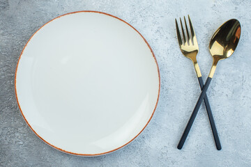Close up shot of elegant cutlery set and empty white soup plate on gray background with distressed surface