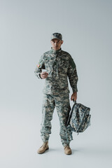 American soldier using smartphone while holding backpack and standing on grey.