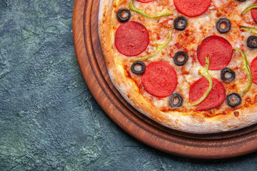 Close up view of delicious pizza on wooden cutting board on the left side on dark blue background with free space