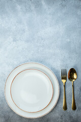Cutlery set and white plates on half dark light gray background with distressed coarse-grained gradient surface