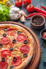 Delicious homemade pizza on wooden board tomatoes ketchup garlics pepper oil bottle green bundle on dark background in half shot