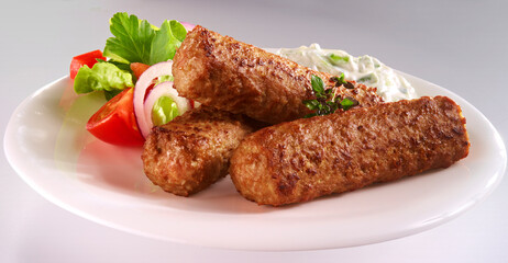 Cevapcici mit Gemuesebeilage und Dip auf weissem Porzellanteller