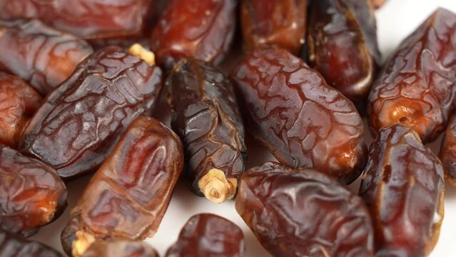 Closeup view 4k stock video footage of tasty sweet dried turkish dates isolated on white plate background. Fruits spinning around slowly. Food video background