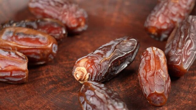 Close up view 4k stock video footage of tasty sweet dried turkish dates isolated. Big dates slowly falling down on brown plate. Food video background