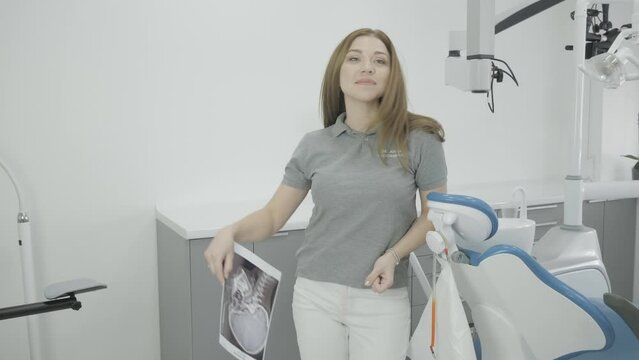 Female dentist in the office of a dental clinic, throws x-ray pictures of teeth, jaw and smiling while looking at the camera
