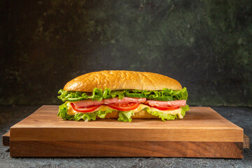 Delicious homemade sandwich on wooden cutting board on black distressed background