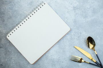 Elegant bright cutlery set and spiral notebook on isolated gray ice background