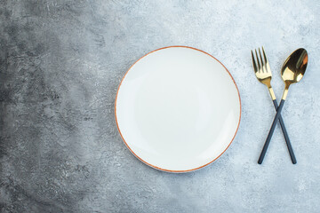 Elegant cutlery set and empty white soup plate on the left side on gray background with distressed...