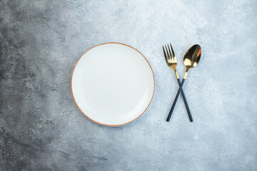 Elegant cutlery set and empty white soup plate on gray background with distressed surface