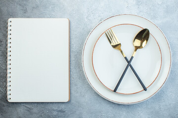 Elegant cutlery set on empty white soup plate in two sizes and notebook on gray background with...