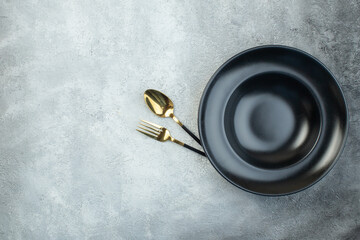 Elegant cutlery set under black dinnerware set on isolated gray ice background with free space - obrazy, fototapety, plakaty