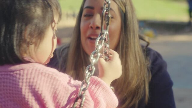 CU Mother swinging daughter (2-3) with Down syndrome on swing