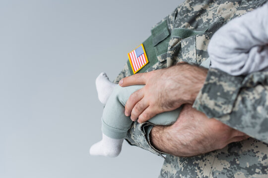cropped view of American serviceman in uniform holding newborn baby isolated on grey.