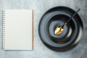 Elegant spoon on black dinnerware set and spiral notebook on isolated gray ice background with free space