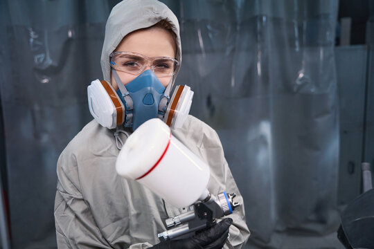 Attentive woman worker in respirator holding spray gun indoors - Powered by Adobe