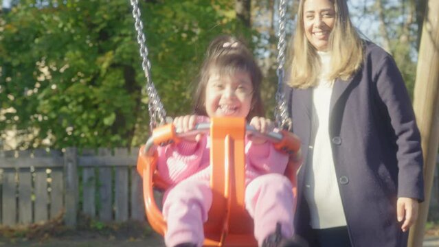 MS Mother swinging daughter (2-3) with Down syndrome on swing