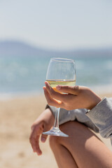 Young beautiful woman hold glass of wine sitting in sea wave foam over nature background. Summer...