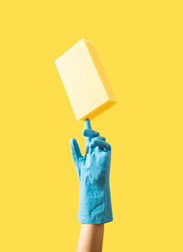 Yellow cleaning sponge balancing on hand with blue latex glove. Minimal concept. Copy space.