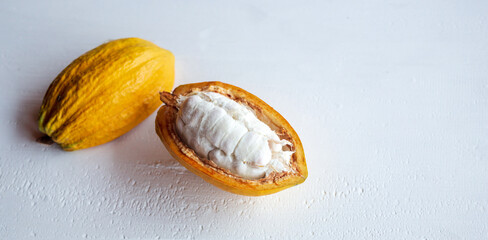 Close-up of ripe fresh slide cocoa pods, half-in cut cocoa fruit revealing the white flesh inside on white wooden background