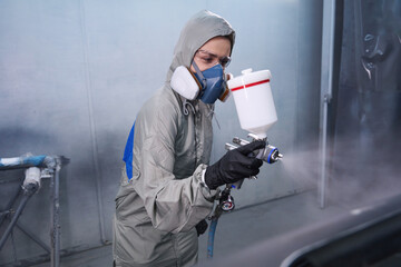 Concentrated woman car technician holding spray gun indoors