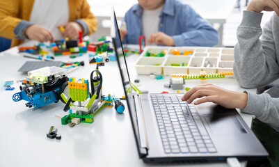 Fototapeta premium Robotics lego programming class. Children construct and code Robot Lego. STEM education using constructor blocks and laptop, remote control joystick. Technology educational development for school kids