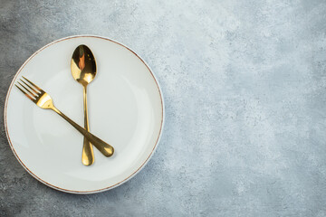 Golden cutlery set on white plate on the right side on gray background with distressed...