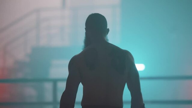 Back shot of a Caucasian bearded boxer man with box gloves on box ring with bokeh background