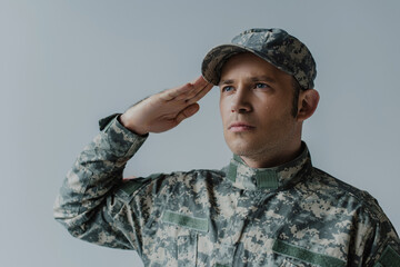 sad military man crying while saluting during memorial day isolated on grey.