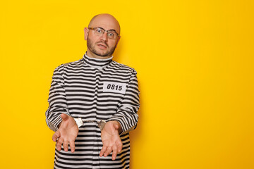 Man wearing prison uniform and handcuffs on yellow background