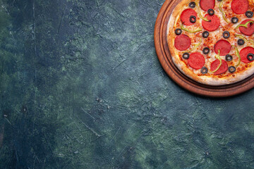 Fototapeta na wymiar Half shot of delicious pizza on wooden cutting board on the left side on dark blue background with free space