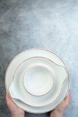Hand holding white dinnerware set on the bottom on half dark light gray background with distressed surface