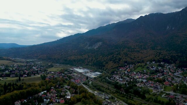 Drone filming cityscape with Suburbs houses and forest trees with green mountains under cloudy sky