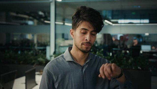 Annoyed irritated Indian Arabian man look at wrist watch check time wait meeting at office frustrated nervous businessman entrepreneur employer client waiting stress being late lateness business meet