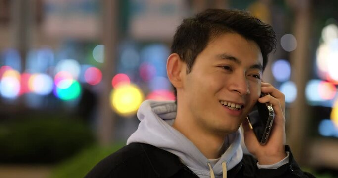 Chinese young man smile and talk on phone call at night urban street with colorful bokeh. slow motion