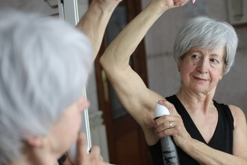 Senior woman applying deodorant in the bathroom 