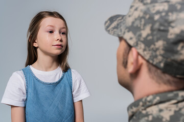 preteen girl looking at brave father in army uniform on blurred foreground isolated on grey.