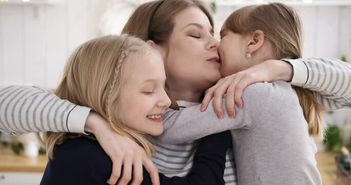Slow motion shot of loving young caucasian mother embracing and kissing cute daughters at home