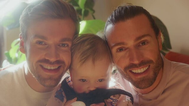 CU Portrait of two smiling men with baby daughter (18-23 months) in living room