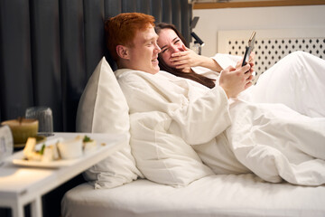 Laughing newlyweds are relaxing in a hotel room