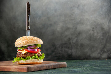 Knife in tasty meat sandwich on wooden cutting board on the right side on isolated dark background